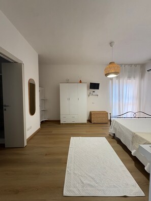 Ein Schlafzimmer mit Bett, Kleiderschrank, Fernseher, einem Korb aus Weidengeflecht und einer Pendelleuchte.