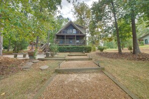A two-story cabin with a porch, surrounded by trees and a gravel pathway.
