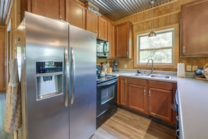A kitchen with wooden cabinets, a stainless steel refrigerator, a stove, and a window with a view.