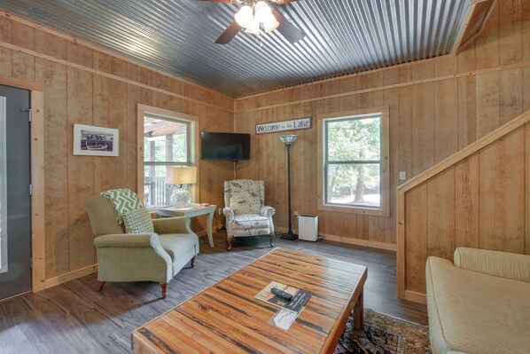 A cozy cabin interior with a wooden floor, a sofa, a chair, a television, and a sign that reads 'Welcome to the Lake.'