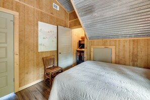 A bedroom with a wooden ceiling, a bed with a quilt, a wooden chair, and a wardrobe.