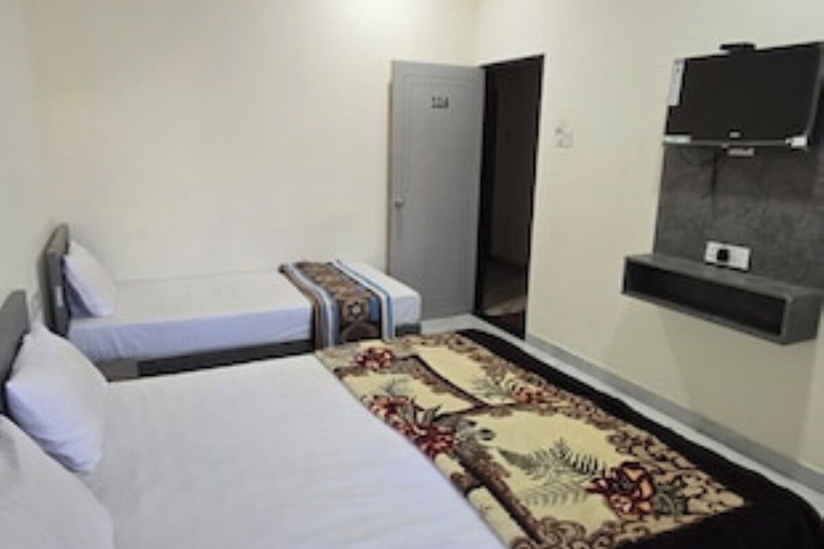 A hotel room with two beds, a ceiling fan, a television, and a door.