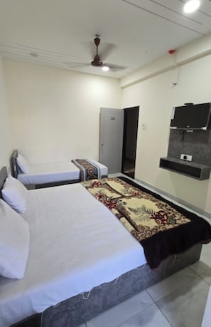 A hotel room with two beds, a ceiling fan, a television, and a door. - Mahesh Bhavan Dwarka (Dwarka)