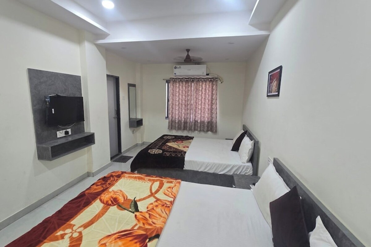 A hotel room with two beds, a television, an air conditioning unit, and a window with curtains.