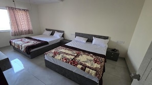A hotel room with two beds, a bedside table with a phone, and a window with curtains. - Mahesh Bhavan Dwarka (Dwarka)