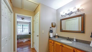 A hallway leading to a bedroom with a ceiling fan, a bathroom with a sink, mirror, and towel rack.