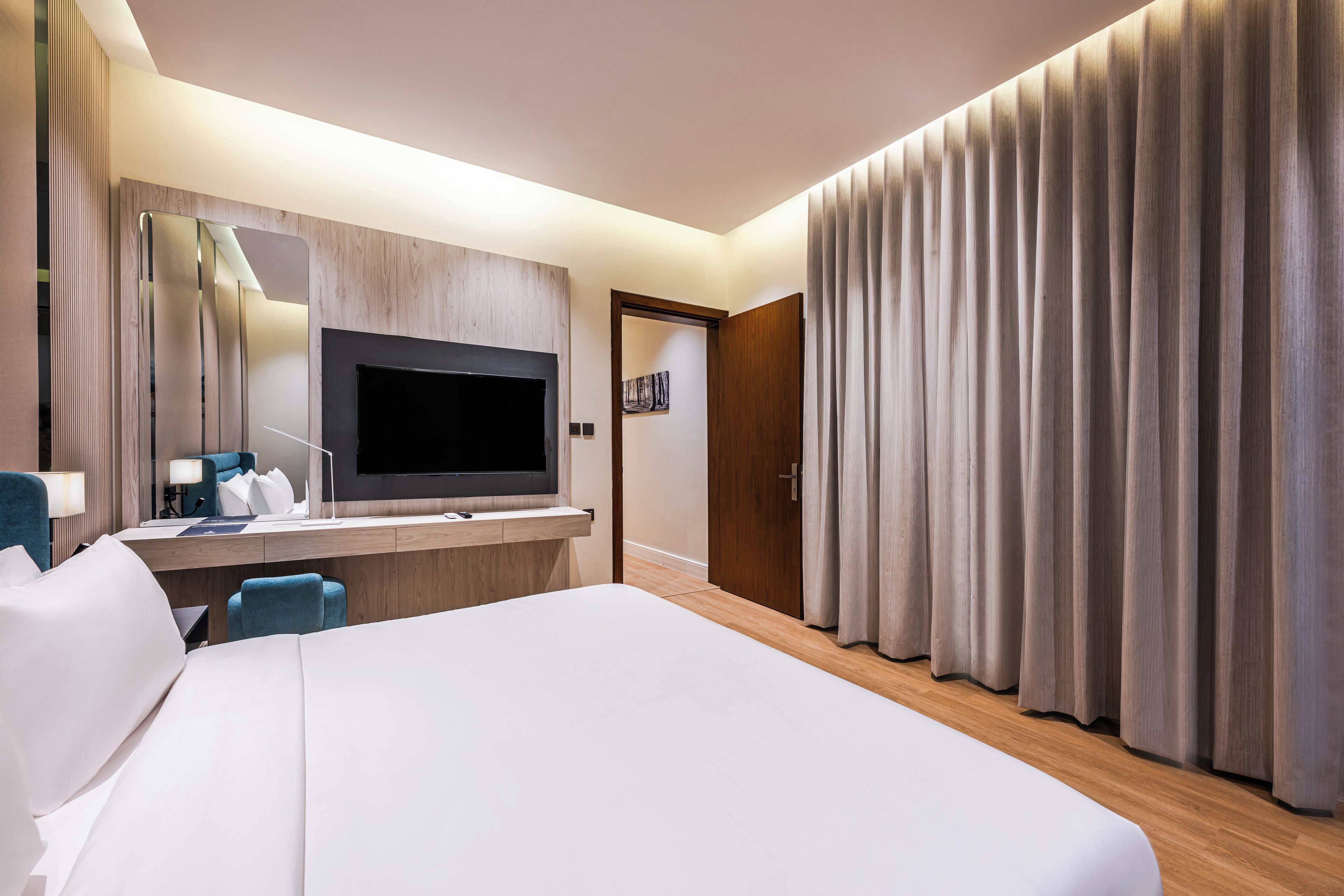 A hotel room with a large bed, a desk with a flat-screen TV, a mirror, and a door with curtains.