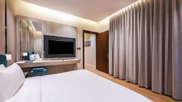 Habitación de hotel con una cama grande, un escritorio, un televisor de pantalla plana, un espejo y una puerta con cortinas.