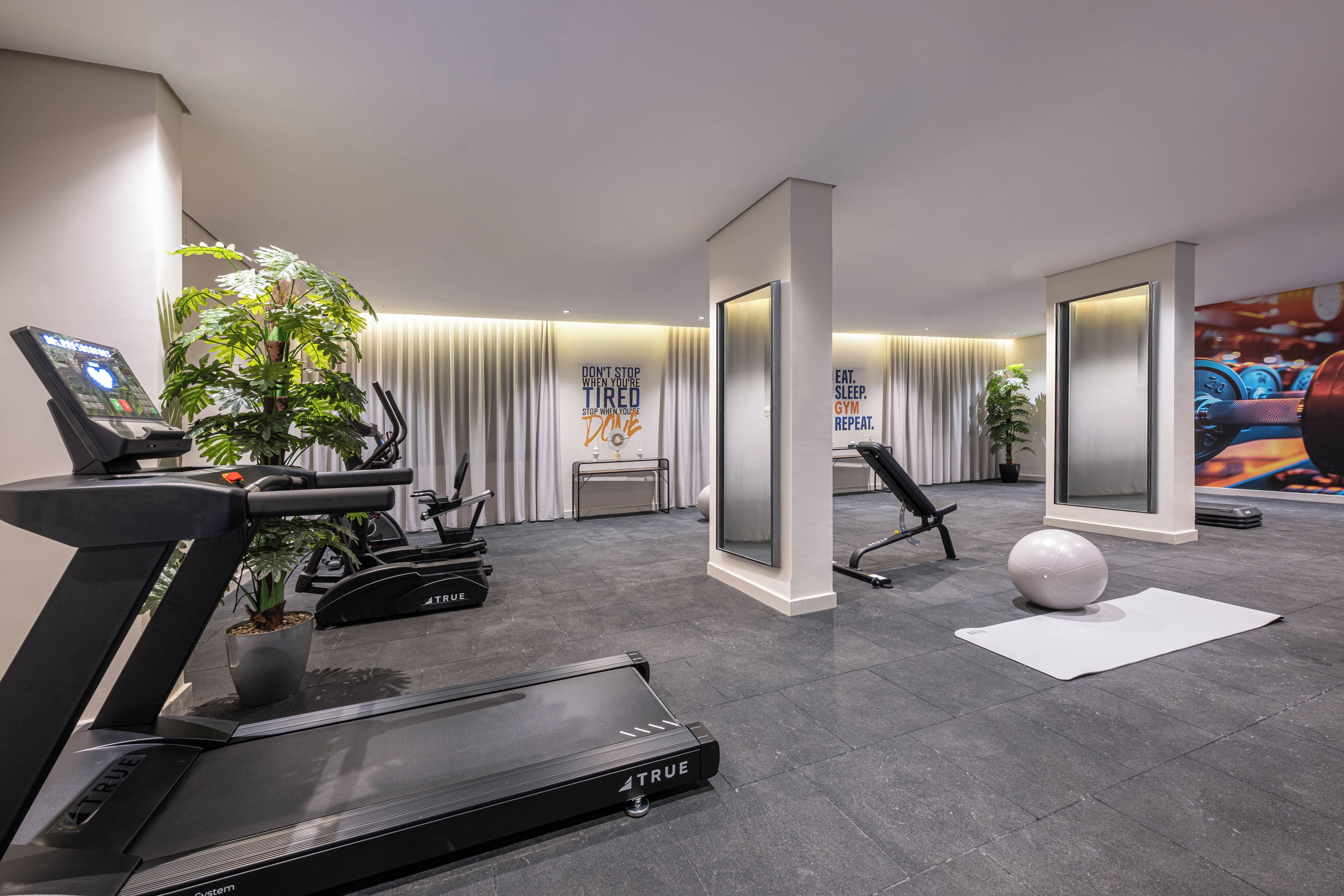 A modern gym with exercise equipment, a treadmill, a stationary bike, and a mirror wall.
