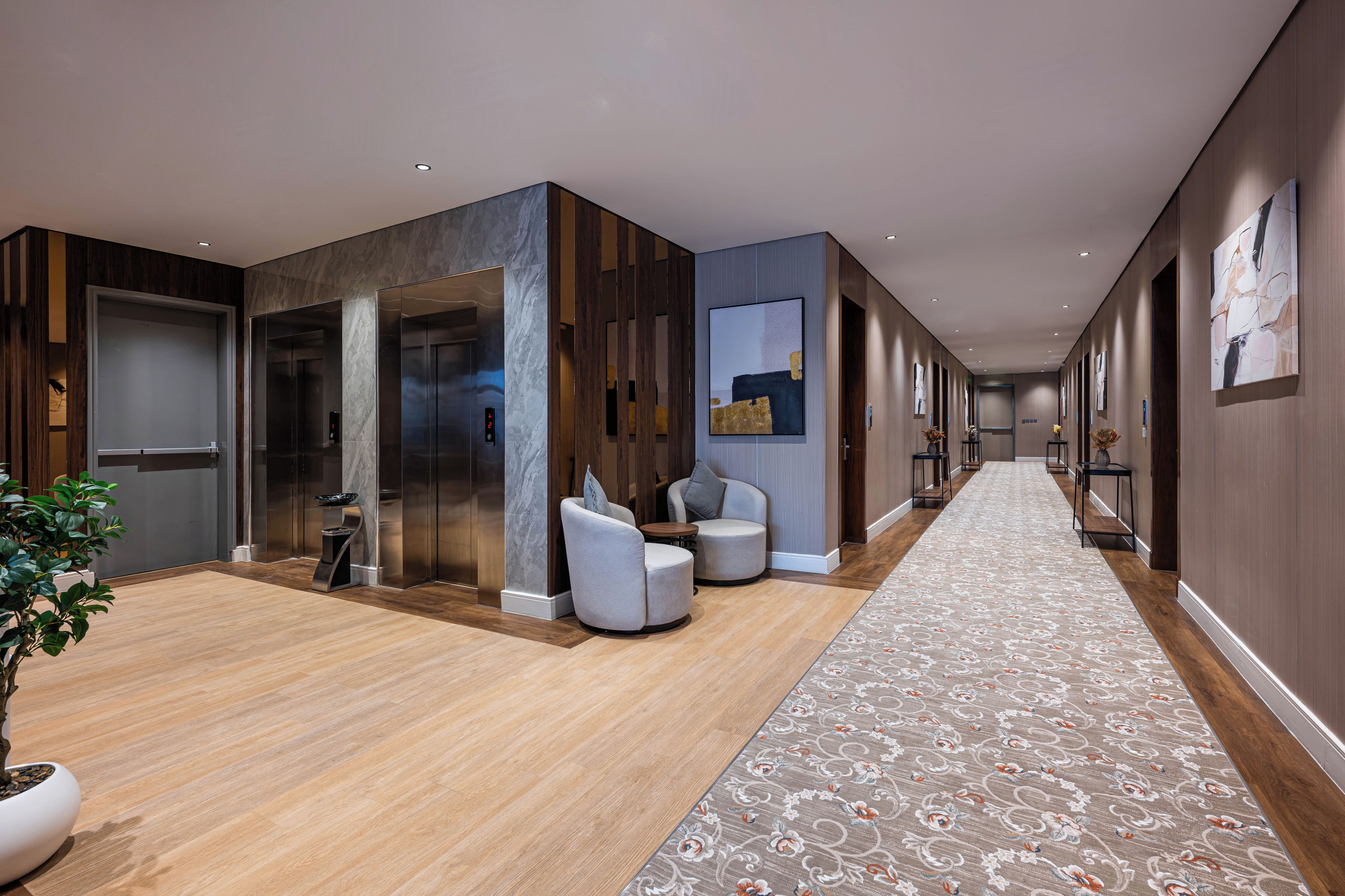 A modern hotel lobby with a wooden floor, seating area, and an elevator.