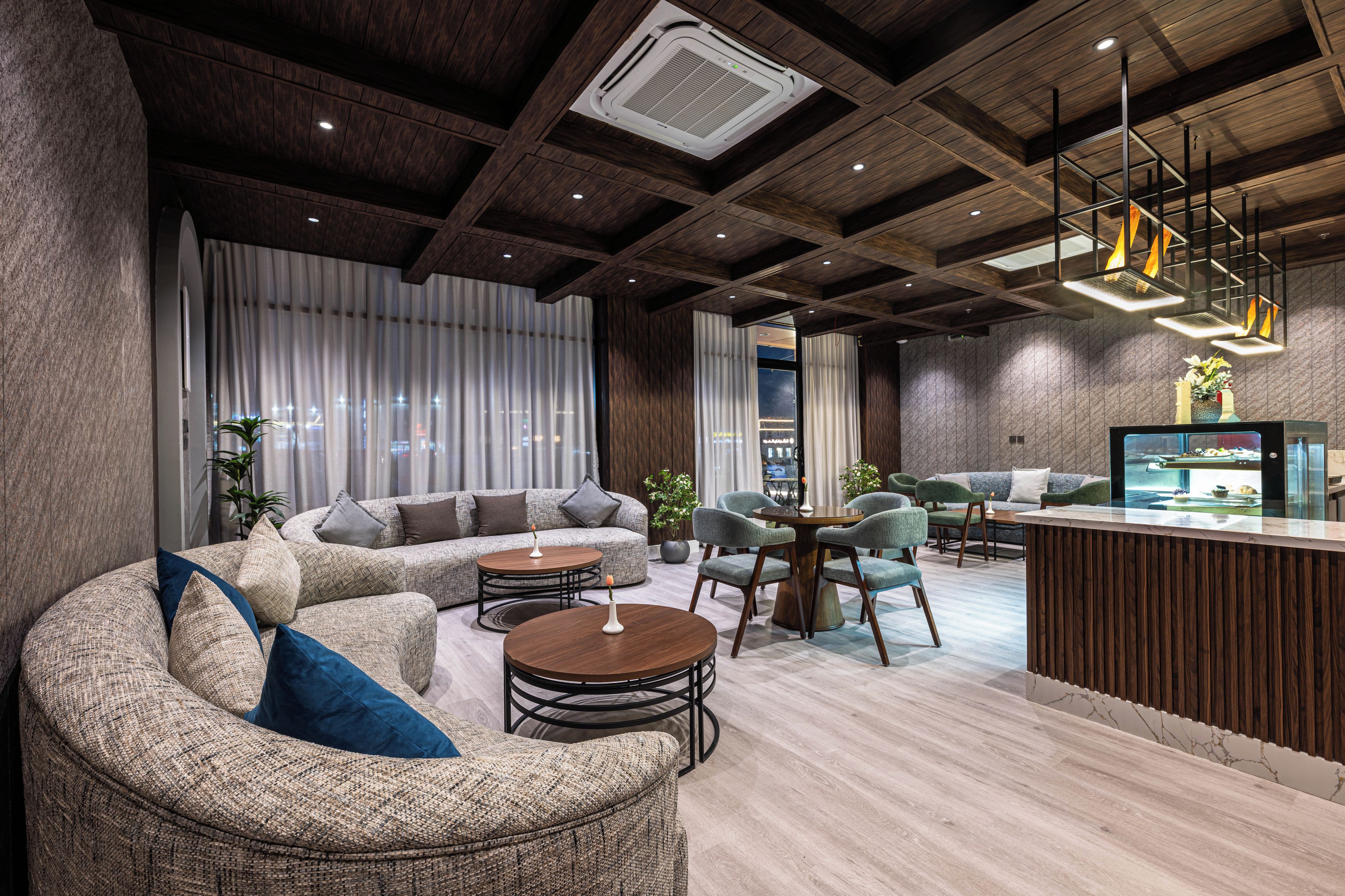 A modern lounge area with a sofa, chairs, a round table, and a bar.