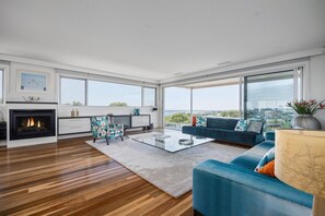 A modern living room with a fireplace, a sofa, a coffee table, and large windows offering a city view. - Stanley House Mt Martha. (Mount Martha)