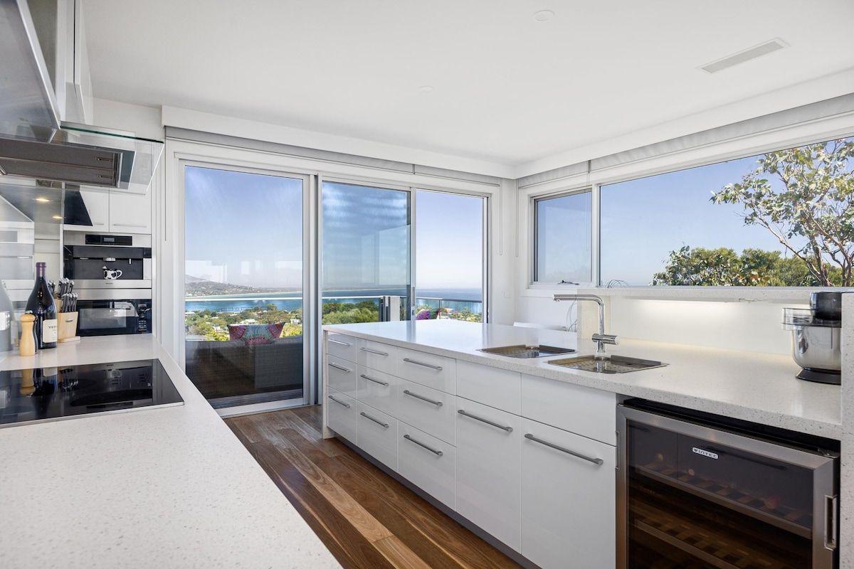 A modern kitchen with a large window, a dishwasher, and a view of the sea.