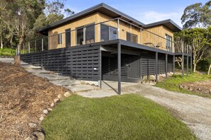 Ein modernes, zweistöckiges Haus mit Flachdach, großen Fenstern und einer überdachten Terrasse mit Metallgeländer.