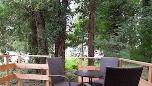 Een houten terras met rieten stoelen en een tafel, omgeven door bomen.