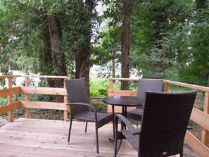Una terraza de madera con sillas de mimbre y una mesa, rodeada de árboles.