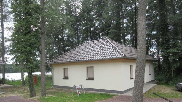 Een laag gebouw met tegels op het dak, omringd door bomen en een grindpad.