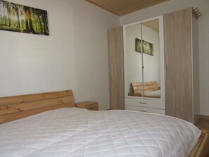 Un dormitorio con una cama, una mesita de noche, un armario con espejo y un cuadro en la pared.