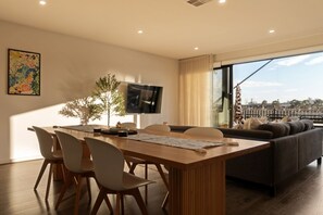 Een moderne woonkamer met een eethoek, een flatscreen televisie aan de muur en een groot raam met uitzicht over de stad.