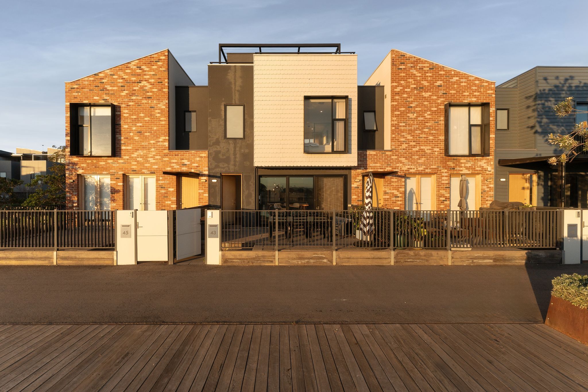 A modern two-story residential building with a brick facade, large windows, and a gated entrance.