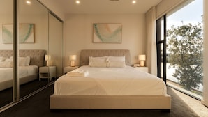 Un dormitorio moderno con una cama grande, dos mesitas de noche, un espejo y vistas a árboles a través de una ventana.