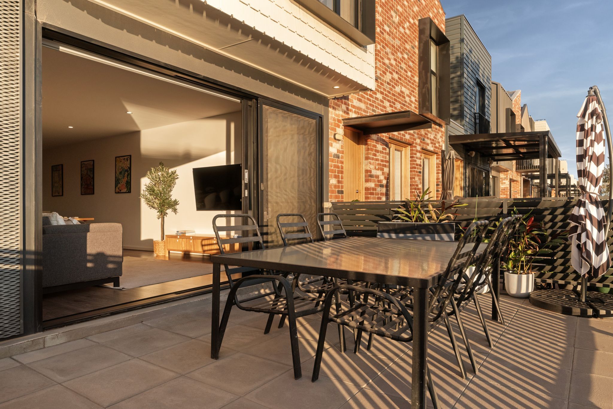 An outdoor patio with a dining table and chairs, a sofa, and a TV mounted on the wall.