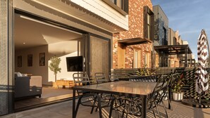 Un patio exterior con una mesa y sillas de comedor, un sofá y un televisor montado en la pared.