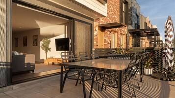 An outdoor patio with a dining table and chairs, a sofa, and a TV mounted on the wall.