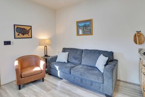 Un salon avec un fauteuil en cuir marron, un canapé gris agrémenté de deux coussins, une lampe, une carte encadrée des États-Unis et un tableau représentant un paysage, également encadré.