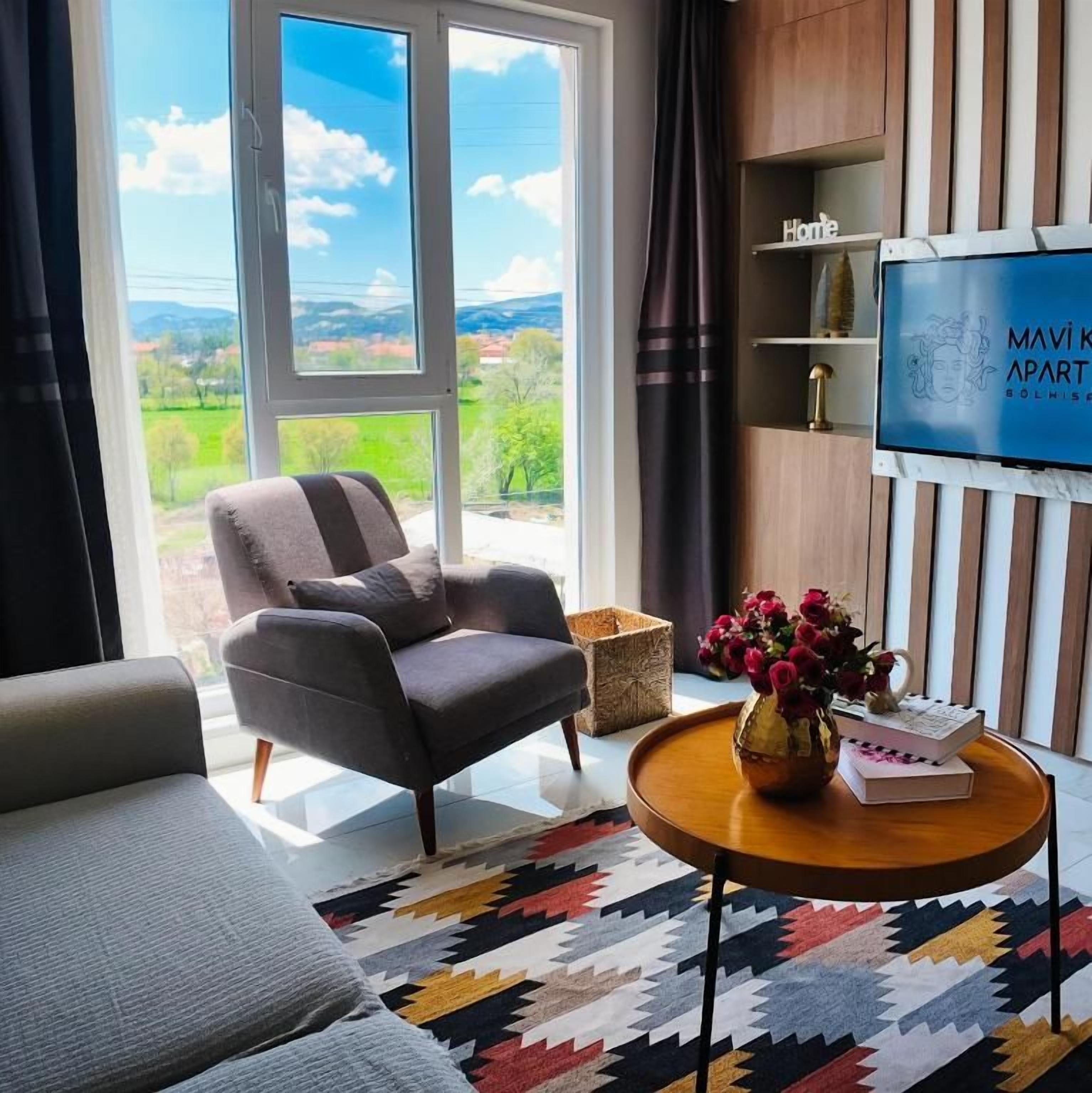 Uma sala de estar moderna com um sofá, poltrona e mesa de centro com um vaso e livros.