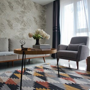 Una sala de estar moderna con un sofá, una mesa de centro con un jarrón de flores, un libro titulado 'CHANEL COLLECTIONS AND CREATIONS' y una alfombra estampada.