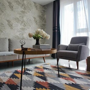 Ein modernes Wohnzimmer mit einer Couch, einem grauen Sessel, einem runden Couchtisch mit einer Blumenvase und einem gemusterten Teppich.