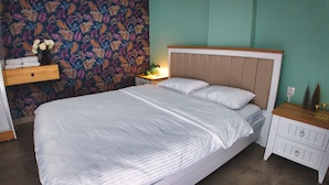 En pænt redt seng med et stribet sengetæppe, et natbord med en lampe, og en væg med et bladmotiv.
