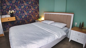Ein ordentlich bezogenes Bett mit einer gestreiften Tagesdecke, ein Nachttisch mit einer Lampe und eine Wand mit einem Blattmuster.