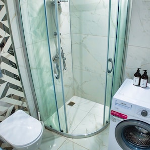 Ein Badezimmer mit einer Duschkabine, einer Toilette und einer Waschmaschine.