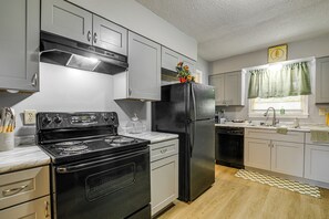 A kitchen with a black stove, stainless steel refrigerator, and white cabinets. - 4 Mi to Graceland! Cozy Home w/ Patio & Yard (Memphis)