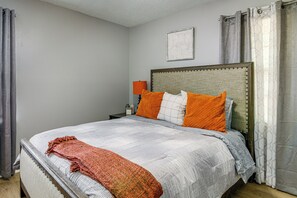 A neatly made bed with a patterned bedspread and pillows, a bedside table with a lamp, and a framed picture on the wall. - 4 Mi to Graceland! Cozy Home w/ Patio & Yard (Memphis)