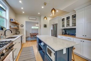 A modern kitchen with white cabinetry, a central island, and a dining area with a view to the outdoors. - Home w/ Office & Yard, 5 Mi to Dtwn Portland! (Portland)