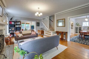 A spacious living room with a sofa, a fireplace, a bookshelf, and a staircase leading to another level. - Home w/ Office & Yard, 5 Mi to Dtwn Portland! (Portland)