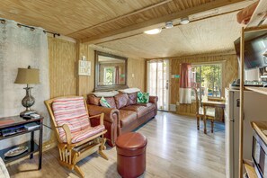 Ein gemütliches Blockhaushaus-Interieur mit Holzbalkendecke, einem braunen Ledersofa, einem gestreiften Sessel, einem kleinen Tisch und einem Fernseher.
