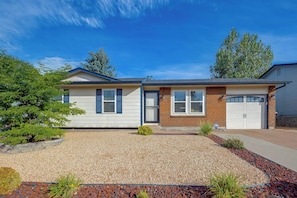 A two-story house with a front garage, a gravel driveway, and a landscaped front yard. - Furnished Stay Near Peterson Space Force Base (Colorado Springs)