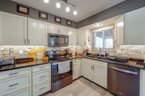 A modern kitchen with white cabinetry, a stainless steel range, a microwave, and a large window with blinds. - Furnished Stay Near Peterson Space Force Base (Colorado Springs)