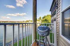 A balcony with a view of a river, a grill, and a house with a screened porch.