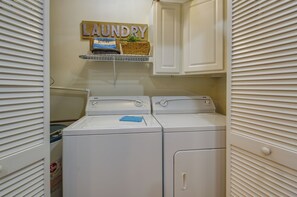 A laundry room with two front-loading washing machines, a shelf with a 'Laundry' sign, and a basket with a towel.