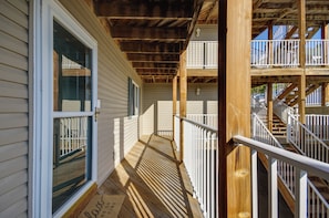 A wooden porch with a white railing, a door with a window, and a staircase leading to a balcony.