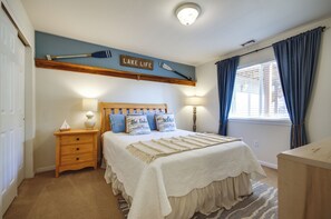 A bedroom with a bed, nightstands, a lamp, a window with curtains, and a wall-mounted sign.