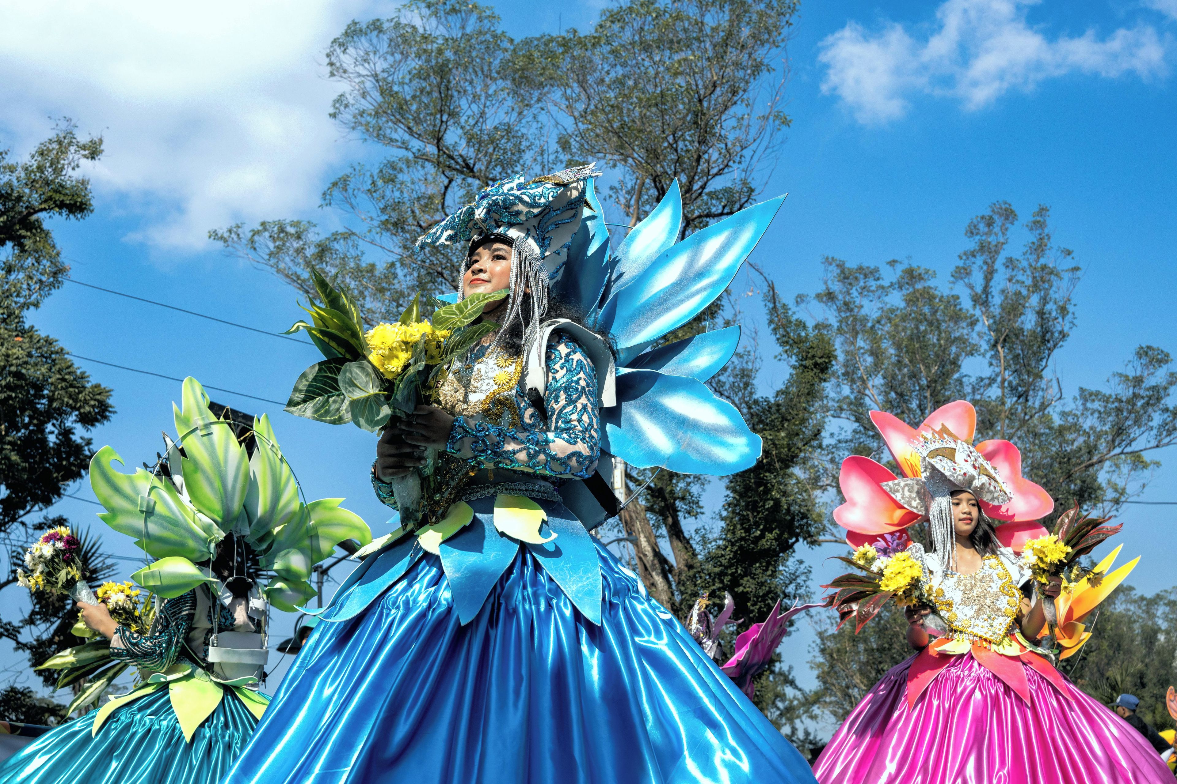 Una persona con un disfraz azul y rosa y una gran tocado de flores.