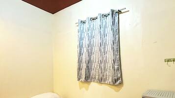 A single bed with pillows and a blanket, a wooden headboard, a wall-mounted curtain, and a black dresser with drawers.