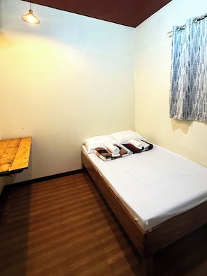 A small, single-bed room with a wooden floor, a bedside table, a hanging light fixture, and a window with a curtain. - Iyaman Balbalays Backpackers Inn  (Baguio)