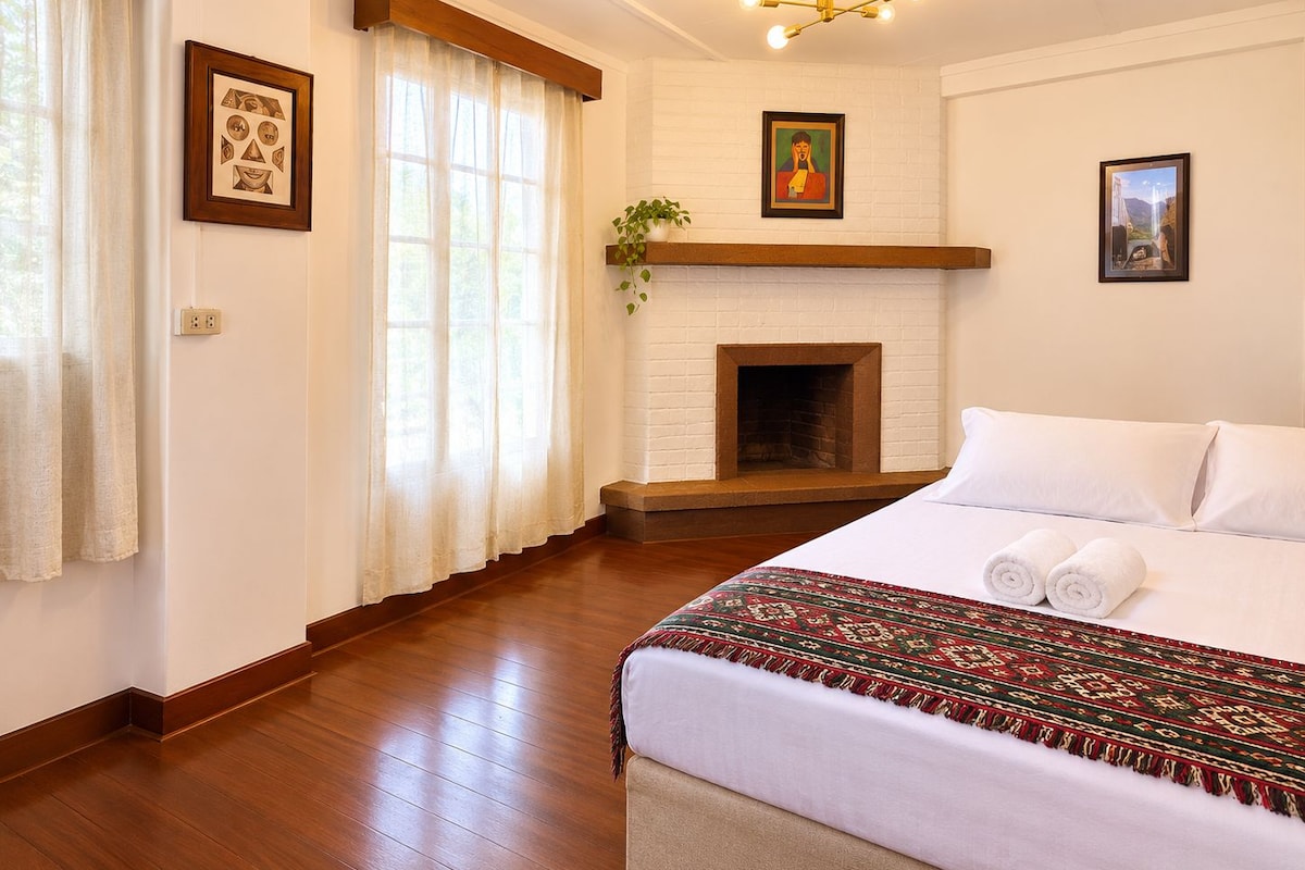Quarto de hotel com cama, lareira e janela com cortinas.